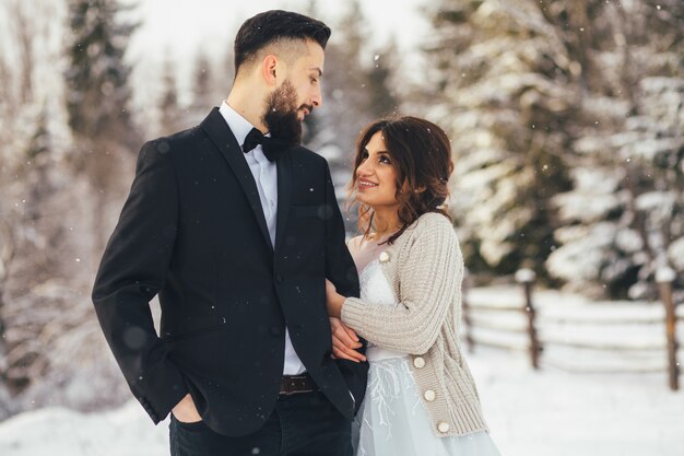 Hombre barbudo y su novia encantadora posan en la nieve en un bosque de invierno mágico