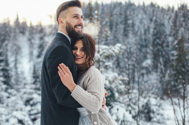 Hombre barbudo y su novia encantadora posan en la nieve en un bosque de invierno mágico