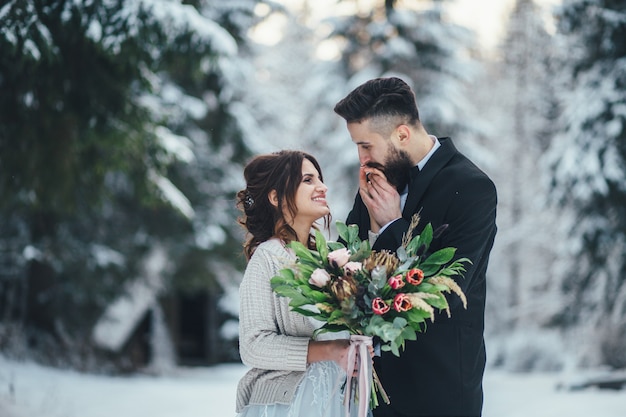 Hombre barbudo y su novia encantadora posan en la nieve en un bosque de invierno mágico