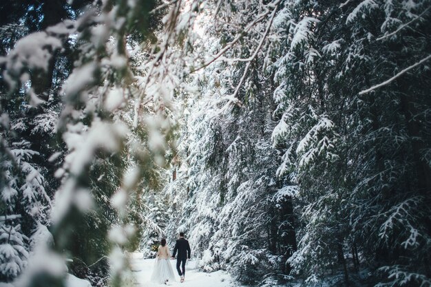 Hombre barbudo y su novia encantadora posan en la nieve en un bosque de invierno mágico