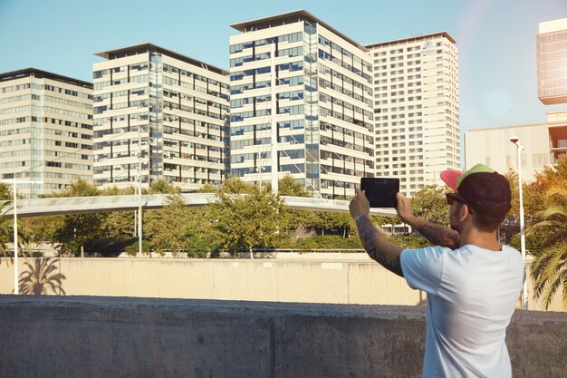 Hombre barbudo con tatuajes tomando una foto de árboles y edificios de la ciudad