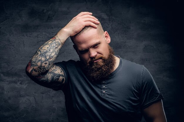 Hombre barbudo toca sus pelos con brazos tatuados.