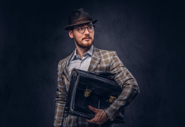 Un hombre barbudo con traje casual con sombrero y gafas sostiene sui