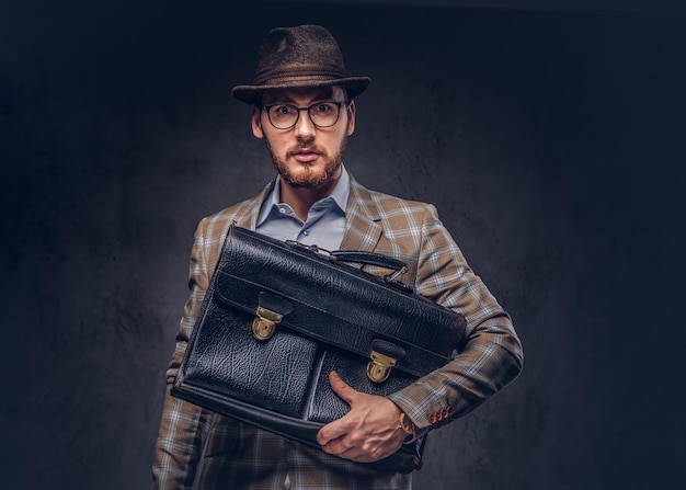 Un hombre barbudo con traje casual con sombrero y gafas sostiene sui