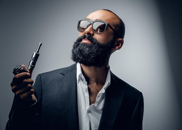 Hombre barbudo con traje y gafas de sol con pipa electrónica.
