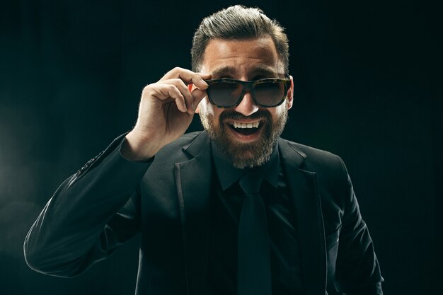 hombre barbudo con traje. Hombre de negocios elegante sobre fondo negro. Hermoso retrato masculino. Joven emocional.