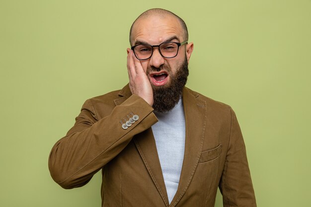 Hombre barbudo en traje marrón con gafas mirando confundido y disgustado