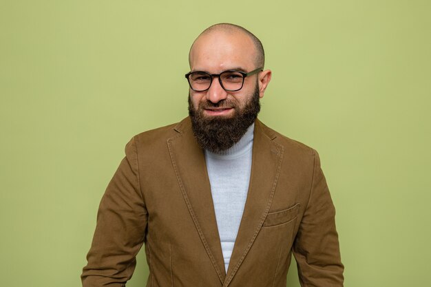 Hombre barbudo en traje marrón con gafas mirando con una sonrisa en la cara feliz
