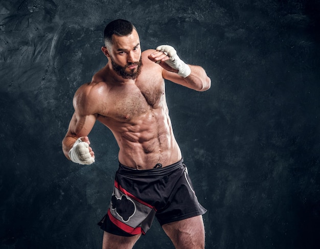 Hombre barbudo varonil con hermoso torso musculoso está posando para el fotógrafo en el fondo oscuro.