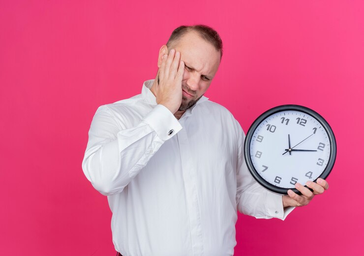 Foto gratuito hombre barbudo vestido con camisa blanca con reloj de pared mirando confundido parado sobre pared rosa