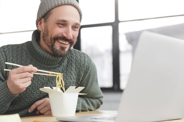 Hombre barbudo vestido con un suéter caliente de punto y un sombrero almorzando