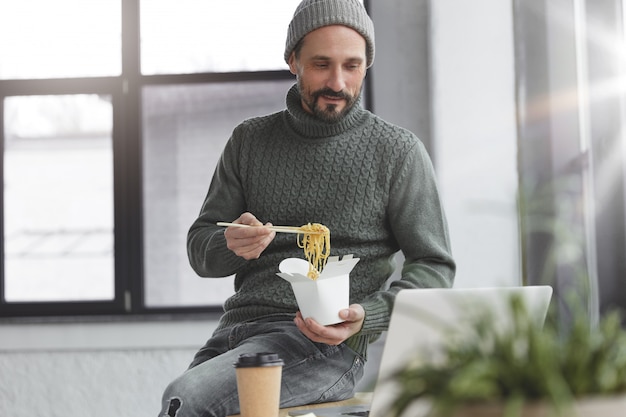 Hombre barbudo vestido con un suéter caliente de punto y un sombrero almorzando