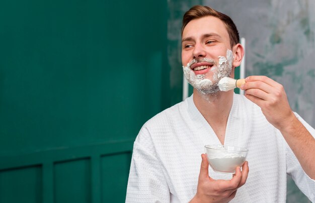 Hombre en bata de baño aplicando espuma de afeitar en la cara con espacio de copia