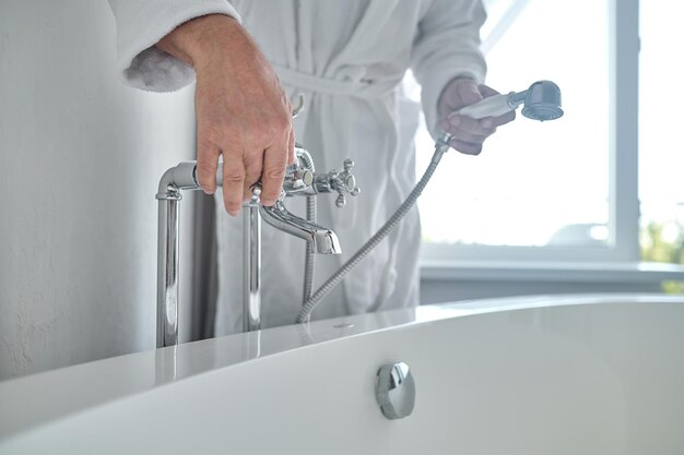 Hombre en una bata de baño de felpa blanca llenando la bañera con agua