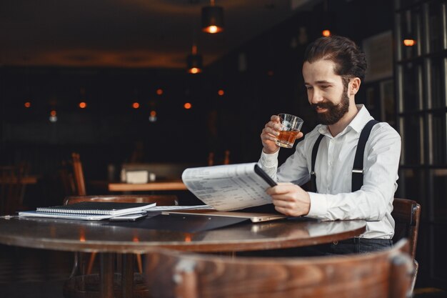 El hombre bebe whisky. El hombre de negocios lee documentos. Director con camiseta y tirantes.