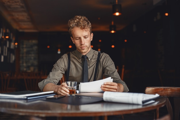 El hombre bebe whisky. El hombre de negocios lee documentos. Director con camiseta y tirantes.