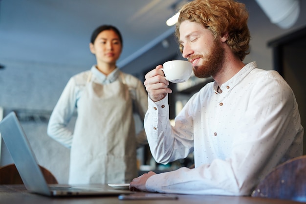 Hombre bebiendo café o té mientras trabajaba en la computadora portátil