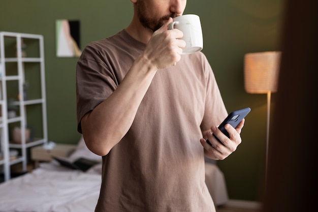 Hombre bebiendo café y revisando correos en el teléfono inteligente