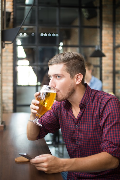 Hombre bebiendo cerveza y utilizando Smartphone en Pub