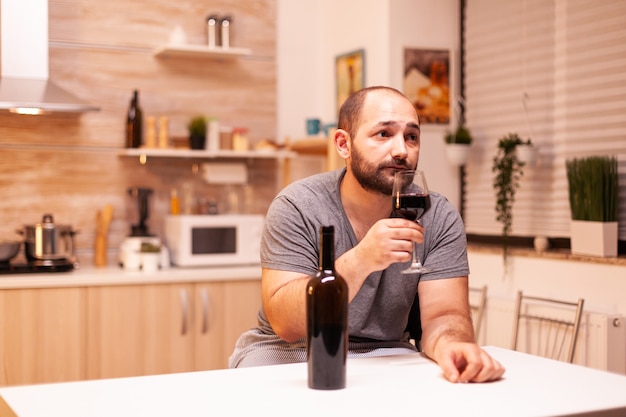 Hombre bebiendo solo en casa debido a la soledad y la tristeza. Enfermedad de la persona infeliz y ansiedad que se siente agotado por tener problemas de alcoholismo.