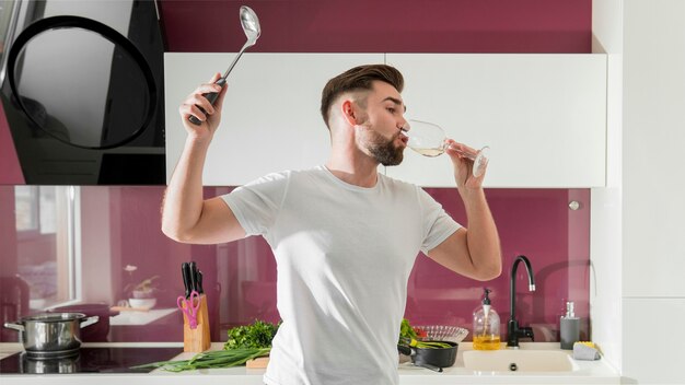 Hombre bebiendo vino y jugando en la cocina plano medio