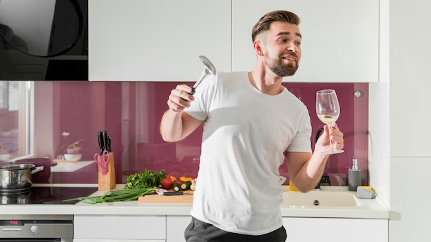 Hombre bebiendo vino y jugando en la cocina
