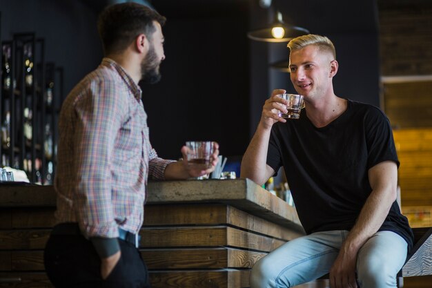 Hombre bebiendo whisky con su amigo en el bar