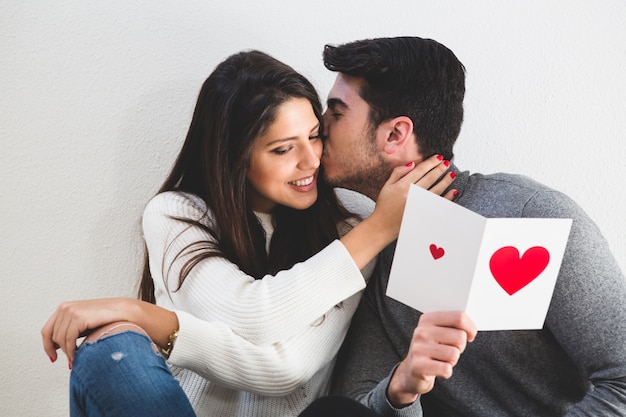 Hombre besándo a una chica en la cara y esta lee una tarjeta postal