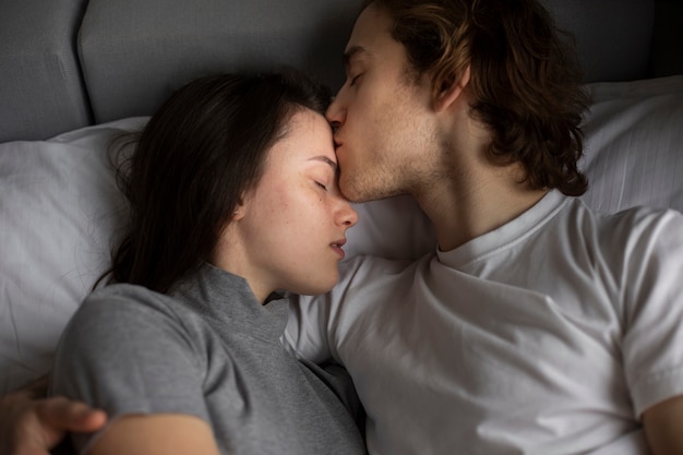 Hombre besando la frente de la mujer en la cama