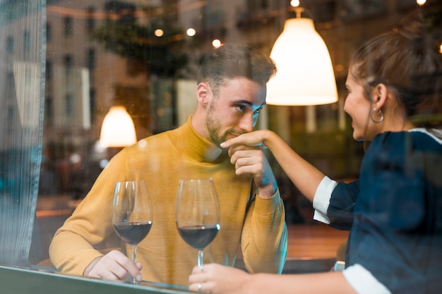 Hombre besando la mano de una mujer alegre con copas de vino en un restaurante
