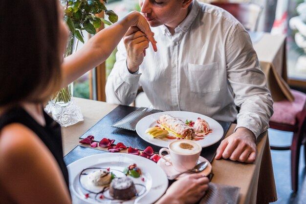 Hombre besando la mano de la mujer en la mesa con postres en café