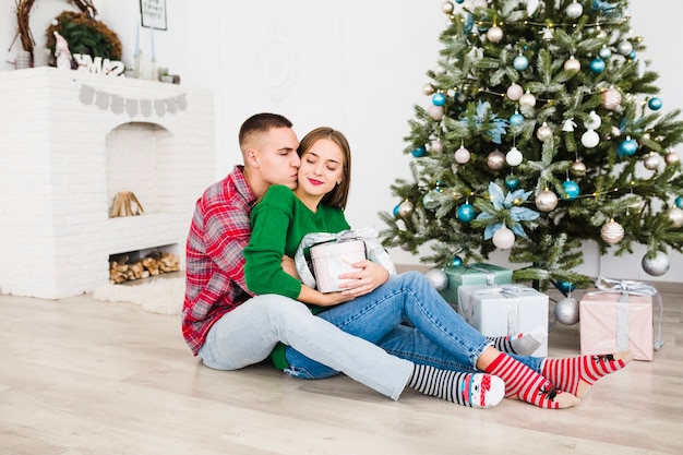 Hombre besando mujer al lado de árbol de navidad