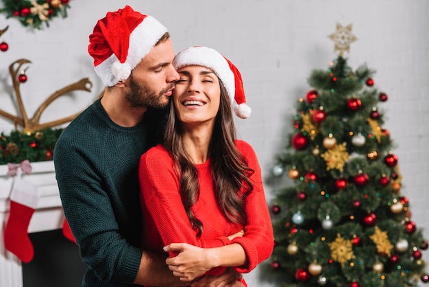 Hombre besando a mujer feliz en sombrero de Navidad