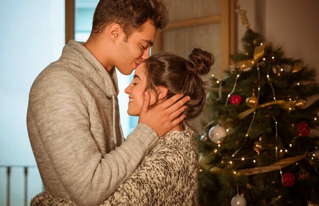 Hombre besando a la mujer en la frente en el árbol de Navidad
