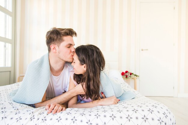 Hombre besando a mujer en frente en la cama