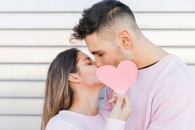 Hombre besando a mujer sosteniendo corazón de papel decorativo