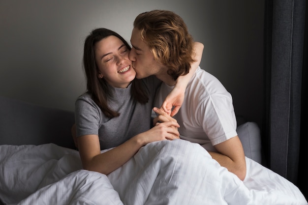 Hombre besando a novia sonriente en la cama