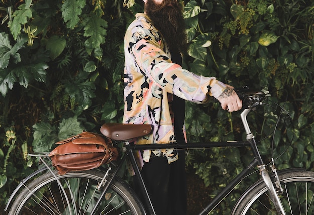 Hombre con la bicicleta de pie delante de las hojas