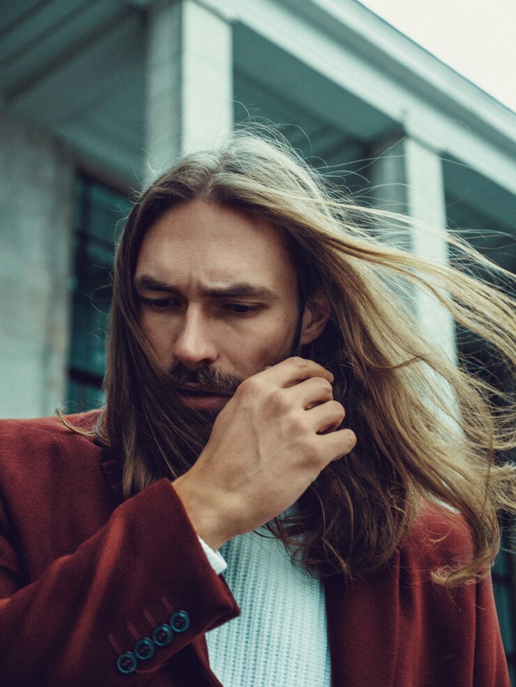 Foto gratuito hombre bien vestido confiado hermoso con la barba que presenta al aire libre que mira lejos. modelo masculino rico de moda en abrigo de invierno rojo y suéter blanco