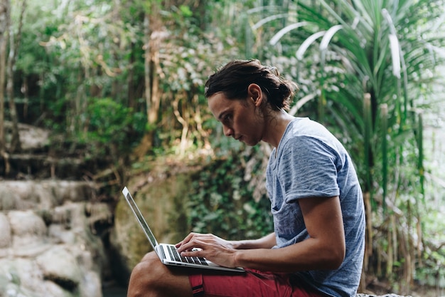 Hombre blanco que usa la computadora portátil en la cascada