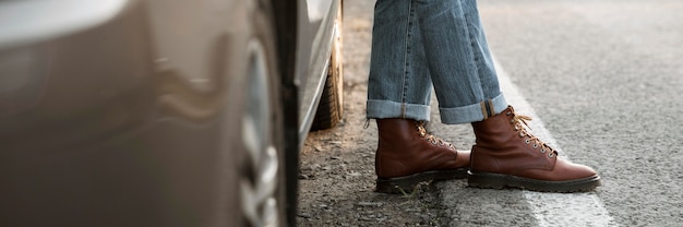 Hombre con botas junto al coche durante un viaje por carretera