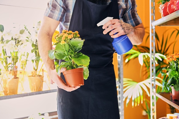 Un hombre con brazos tatuados regando flores en una maceta.