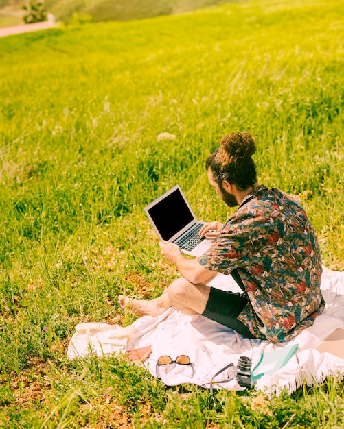 Hombre brunet joven que sostiene la computadora portátil en la naturaleza