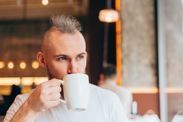 Hombre brutal de apariencia europea en un café por la mañana con una taza de café caliente