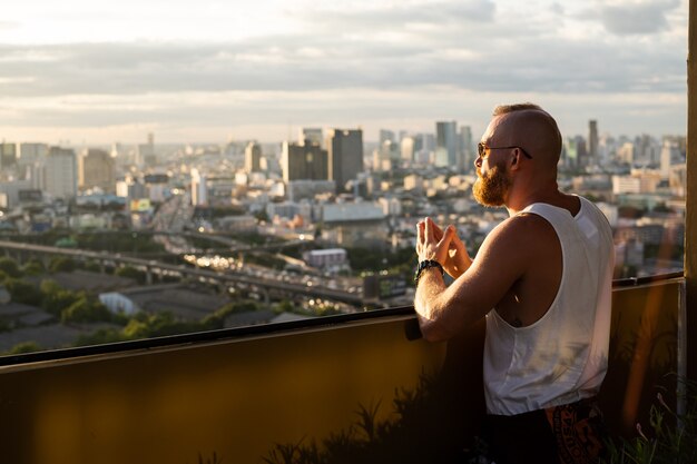 Hombre brutal barbudo guapo caucásico disfrutando de la puesta de sol y vista de la ciudad de Bangkok desde el piso alto