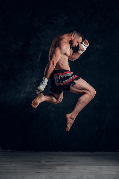 Foto gratuita el hombre en buena forma física está saltando, haciendo ilusión de vuelo antes de golpear un estudio oscuro.