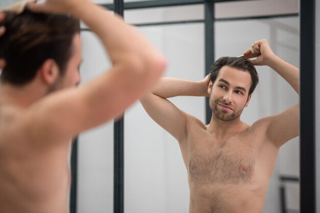Hombre de cabello oscuro cepillando su cabello en el espejo