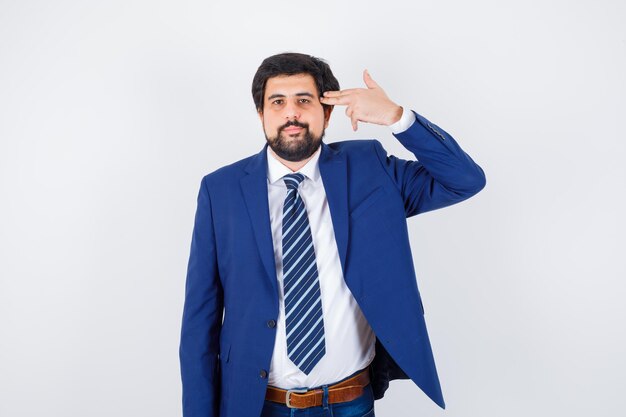 Hombre de cabello oscuro haciendo pistola hacia su sien con camisa blanca, chaqueta azul oscuro, corbata y aspecto aburrido. vista frontal.