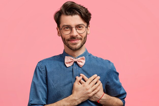 Hombre de cabello oscuro vestido con pajarita rosa y camisa vaquera