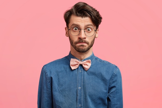 Hombre de cabello oscuro vestido con pajarita rosa y camisa vaquera